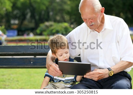 Grandchild teaching to his grandfather to use tablet on a bench