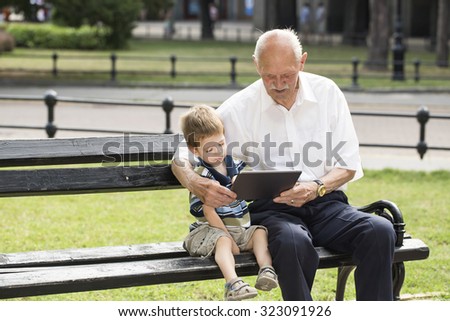 Grandchild and his grandfather using tablet pc on a bench