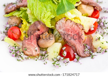 Salad with beef, mushrooms, cucumbers, cherry tomatoes and red onion on a white plate, close-up.