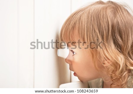 Little girl looks in a curious hole in the fence