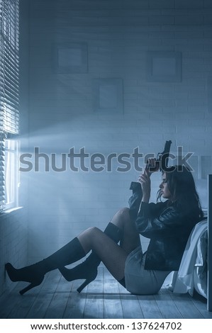 Woman with gun in hand is sitting by the bed in the darkness