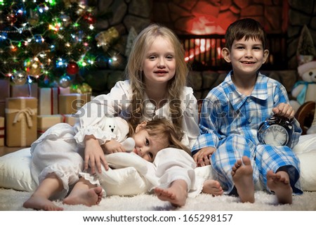 Portrait of children under the Christmas tree by the fireplace
