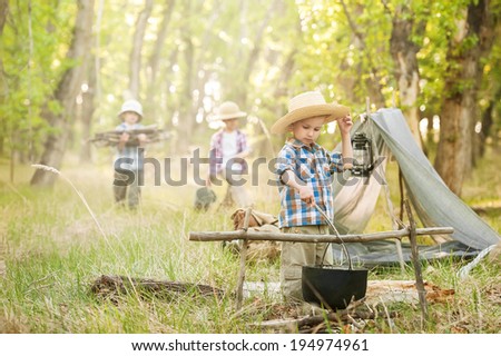 Three little boys staged a halt with a tent and a campfire in the woods in summer sunny day