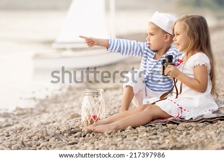 Boy with a girl sitting on the beach with binoculars and looking into the distance on a sunny summer afternoon lake