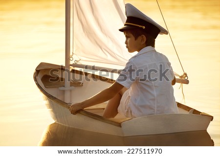Boy seaman floats on a sailing boat at sunset on a warm evening summer
