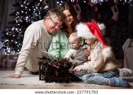 Parents with children write letters to Santa Claus sitting under the Christmas tree by the fireplace