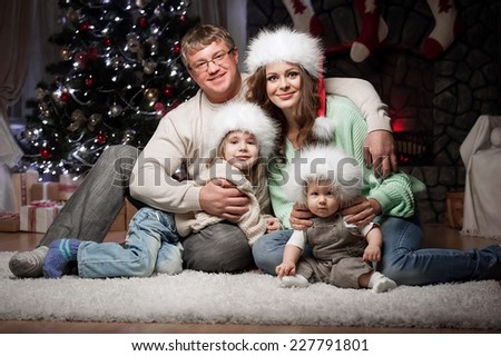 Young family with two children sitting at home New Year\'s Eve by the fireplace and near the elegant tree