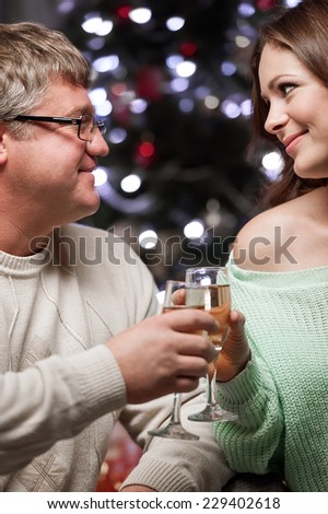 Young couple celebrate Christmas with glasses of champagne sitting by the fireplace and elegant Christmas tree