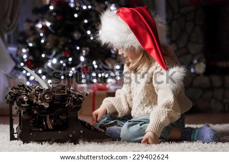 Little girl writes a letter to Santa Claus sitting under the Christmas tree by the fireplace