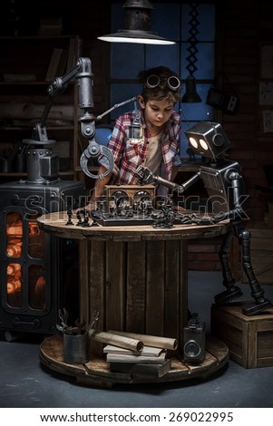 Boy mechanic looks like two robots play a game of chess in the studio in the evening