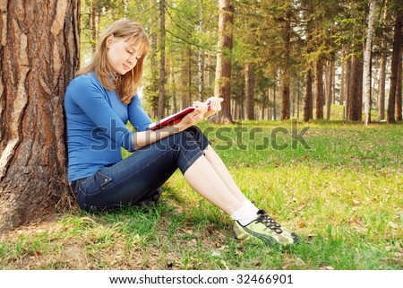 The young girl reads the book under a tree