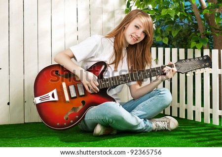 Teenage girl with a guitar at the fence in the garden in summer sunny day