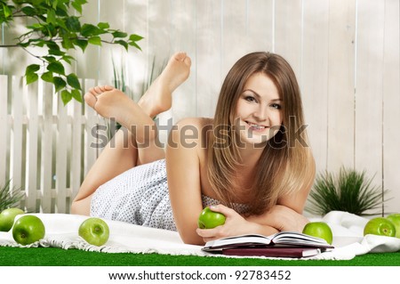Young girl reads a book and eating apples in the garden