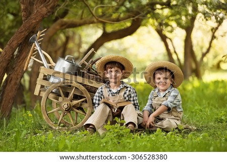 Two boys, gardener resting near a cart with inventory in the garden of spring warm day