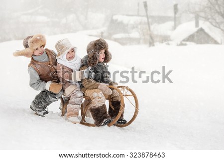 Three small children slide down hills on sleds in winter sunny day