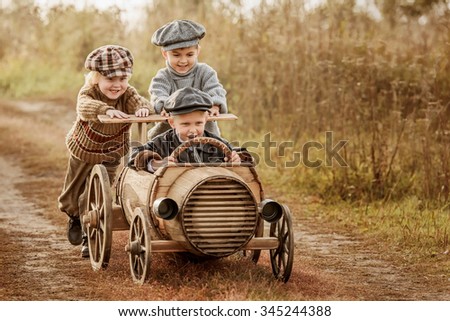 Two young children ride in the third race car from wooden barrels on a rural road autumn evening