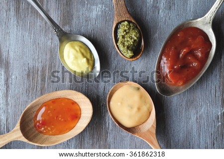Different sauces in spoons on wooden table Top view