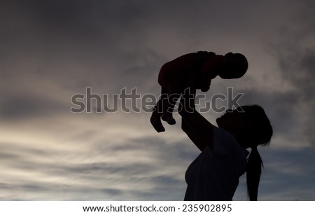 Daughter in her mother\'s arms silhouetted at cloud of bad weather at Thailand. Mother\'s & baby is motion-blurred.