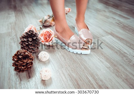 Product photography for pink shining fashion shoes which are exposed on female beautiful legs, combined with pink roses flowers and pine cones. The girl is standing on vintage wooden floor.