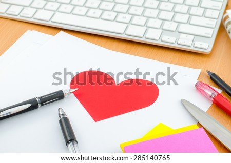 Red heart on white paper with pen on computer desk