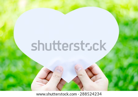 Hand holding white heart paper on blur green grass background - Give heart