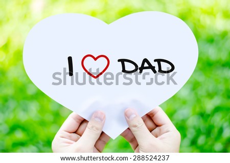 Hand holding white heart paper with I love dad text on blur green grass background - father\'s day