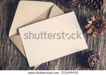 Blank white paper card with brown envelop and pine cones on old wooden table with vintage and vignette tone