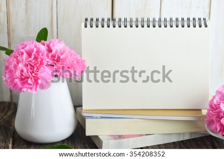 Blank Desk calendar on pile of books with pink carnation flower in white vase on wooden table