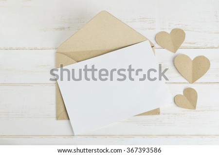 Blank white greeting card with brown envelop and heart tag on old wooden table with soft vintage  tone