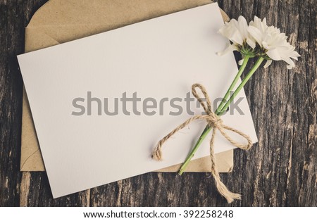 Close up of blank white greeting card with brown envelope and wither Mum flowers on wooden table with vintage and vignette tone