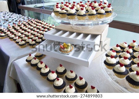Mini cupcake with red heart shaped topping.  The desserts are arranged and displayed in desserts bar at a opened cocktail party.