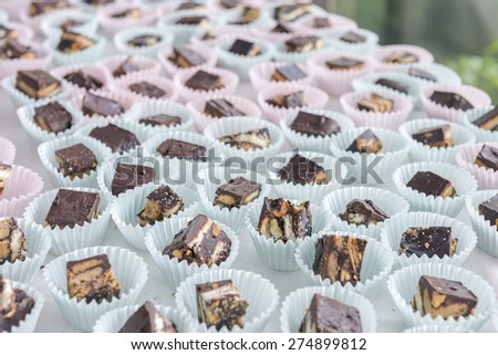 Chocolate crunch cake, cut into pieces and placed in mini paper cake cup.  It is displayed in desserts bar at the opened garden party.