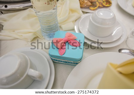 An aqua color gift box with ribbon placed amongst eating utensils on a dining table.