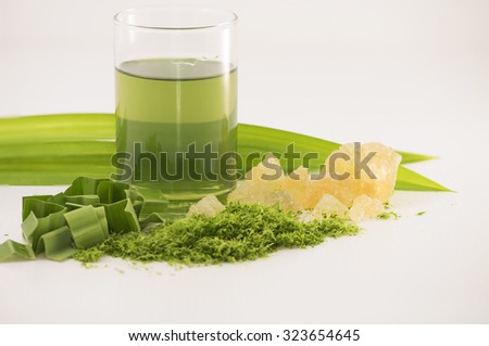 Closeup on green drink.  Some cut pandan leaf, rock sugar and blended leaves at foreground.  Background of blur long pandan leaves on white.