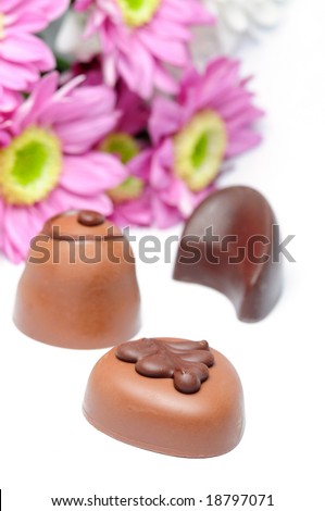Chocolate candies and flowers on white background