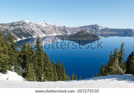 Clear blue water of Crater Lake National Park in Oregon during early spring with some snow left from winter. Wizard Island in the distance.