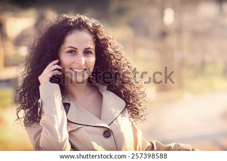 Charming young woman in white jacket reads or texts message to mobile phone in the city. / Vintage style photo with a random white balance, color effects and some fine film noise is added.
