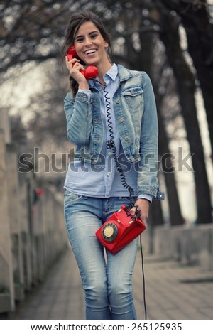 Beautiful young woman talks on a red phone in the city and smiles / Unusual cellphone / Vintage look image with a custom white balance and color effects