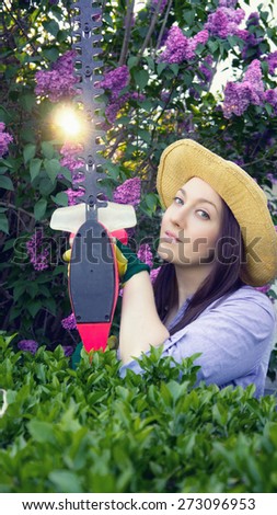 Beautiful young woman works in the garden with a hedge trimmer. / color effects and custom white balance used on this picture.
