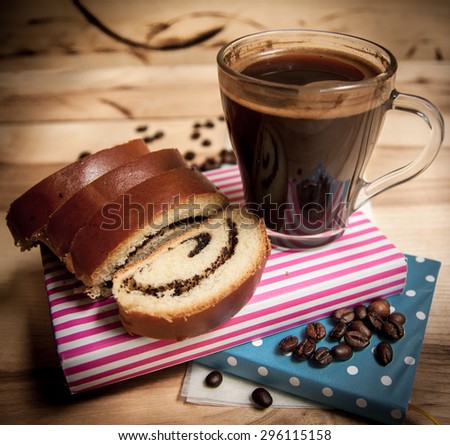 Slice bun with poppy and cup of coffee on wooden table