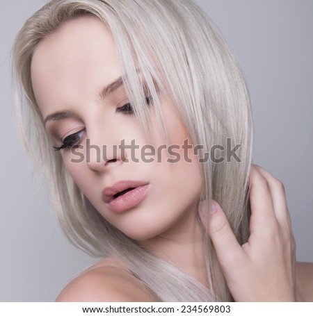 beautiful young woman with clear skin and blonde hair posing on grey background with bracelet