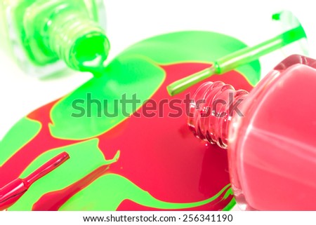Red and green nail polish bottles with nail polish pouring from them on the white background