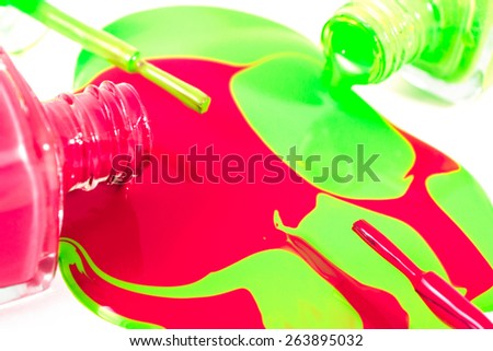 Red and green nail polish bottles with nail polish pouring from them on the white background