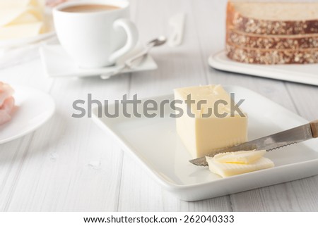 stick of butter on white plate with coffee and bread at the background