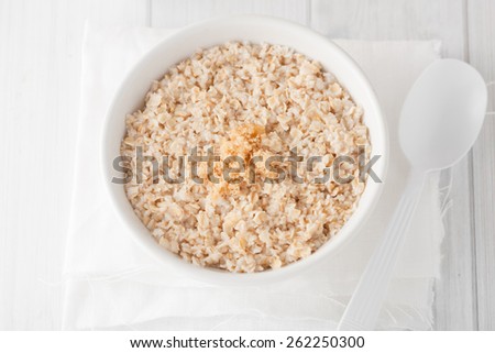 a bowl of cooked oatmeal with brown sugar in white bowl on white background, top view