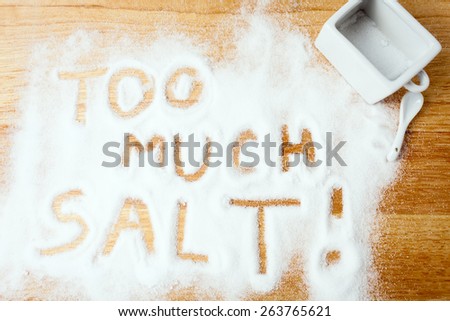 words TOO MUCH SALT handwritten on salt spilled on wooden board