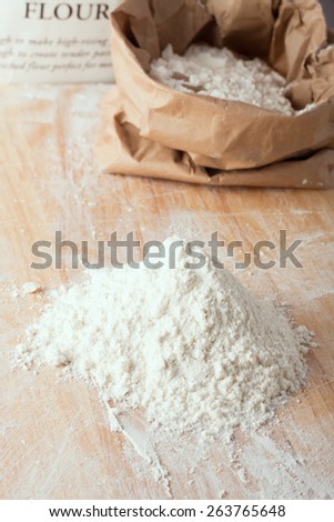 small amount of flour on wooden board with a bag of flour at the background