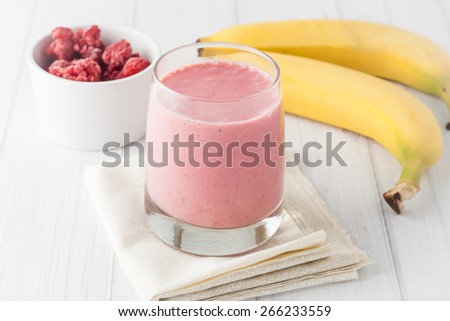 a glass of fresh homemade frozen raspberries and banana smoothie on white background