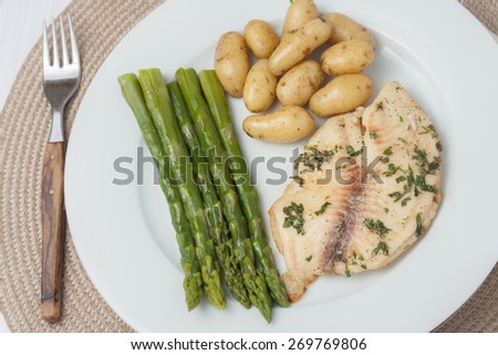 cooked fish with parsley servied with asparagus and baby potatoes on white plate, top view