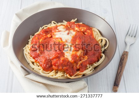 homemade breaded cutlet in tomato sauce and melted cheese over spaghetti in brown bowl on white background